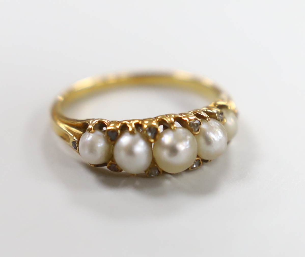 An Edwardian yellow metal and graduated split pearl set half hoop ring, with diamond chip spacers, size M, gross weight 3.1 grams.